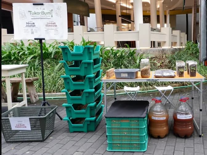 Maggot tower dari krat hijau bertumpuk dan galon eco-enzyme di samping meja pengolahan